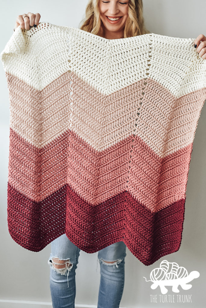 Woman holding a pink, ombre, chevron crochet blanket. Bebe Baby Blanket crochet pattern by The Turtle Trunk