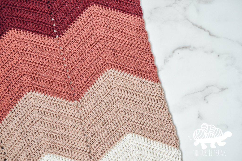 Pink, ombre, and chevron crochet blanket laying on a white surface. Bebe Baby Blanket crochet pattern by The Turtle Trunk