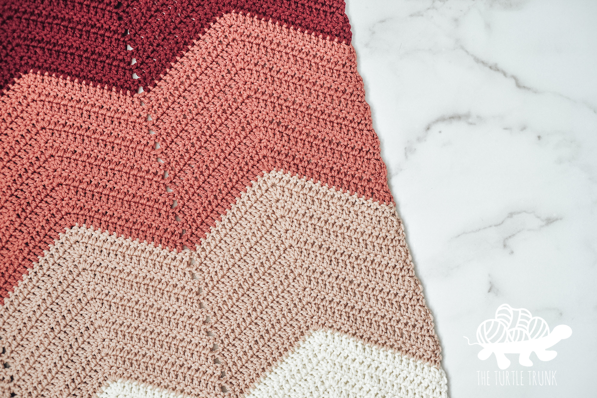 Photo shows a pink ombre and chevron crochet blanket. Crochet pattern is the Bebe Baby Blanket by The Turtle Trunk.