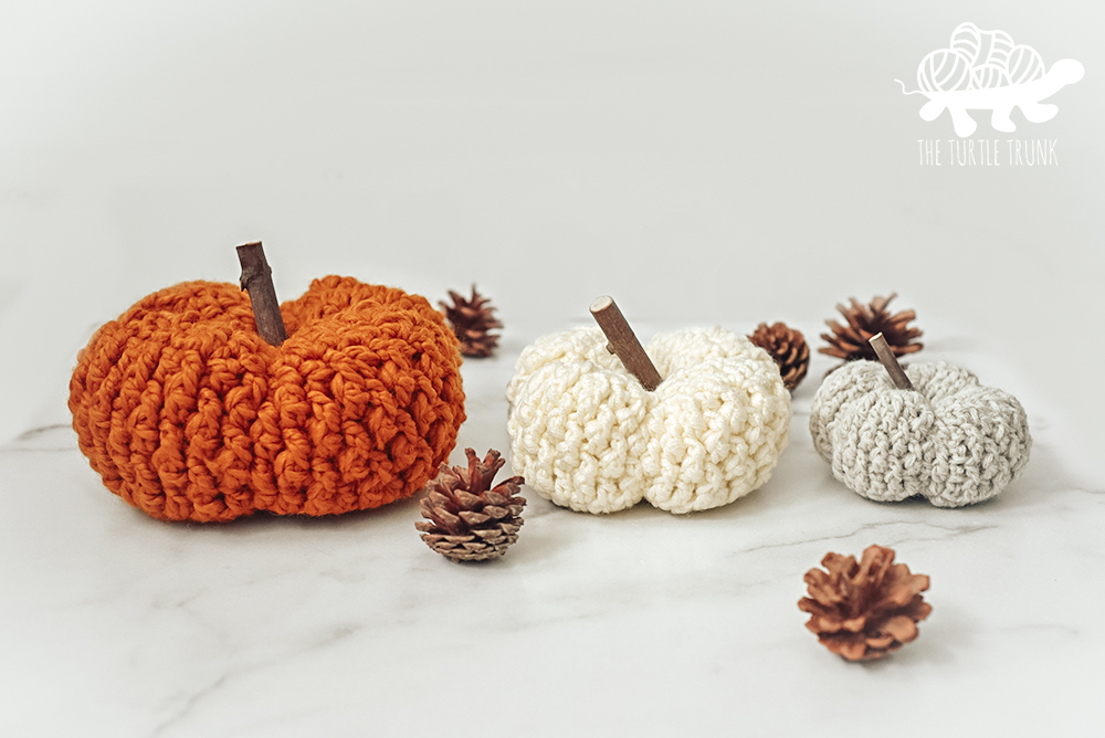 Photo shows 3 crochet pumpkins sitting on a white table top. Crochet pattern is the Country Cottage Pumpkin by The Turtle Trunk.