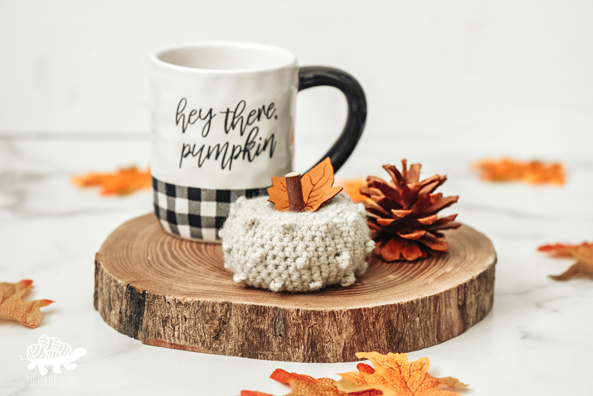 Photo shows a small crochet pumpkin sitting beside a coffee cup on a wood slice. Crochet pattern is the Picot Pumpkin by The Turtle Trunk.