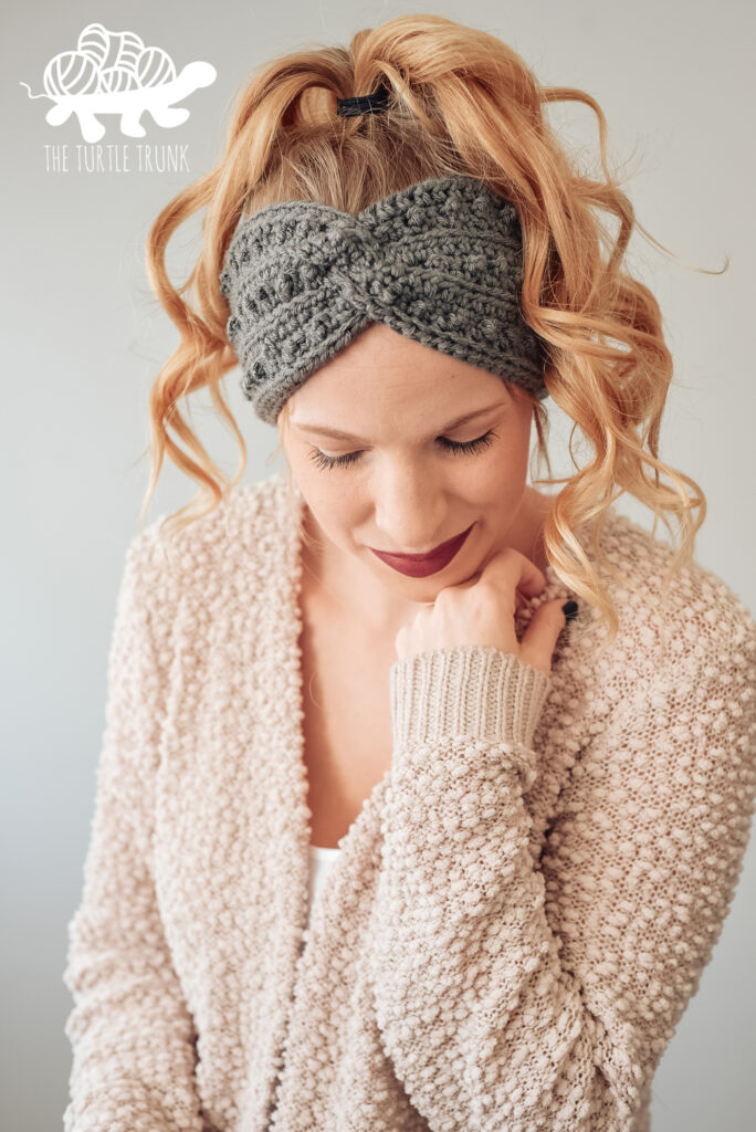 Woman wearing a dark grey, crochet headband. Crochet pattern is the Picot Headband by The Turtle Trunk.