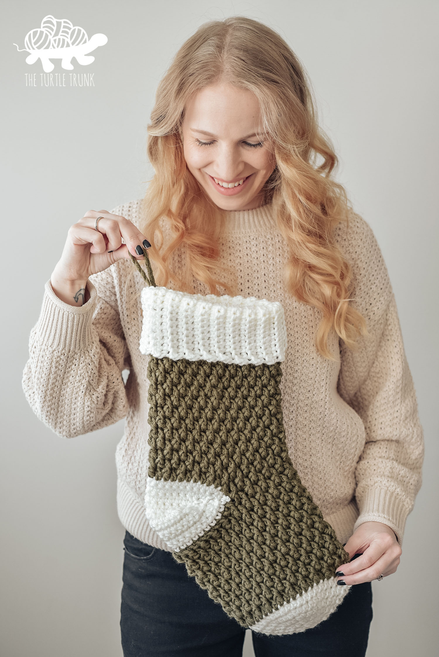 Photo shows a woman holding a green and white crochet Christmas stocking. Country Cottage Stocking by The Turtle Trunk.