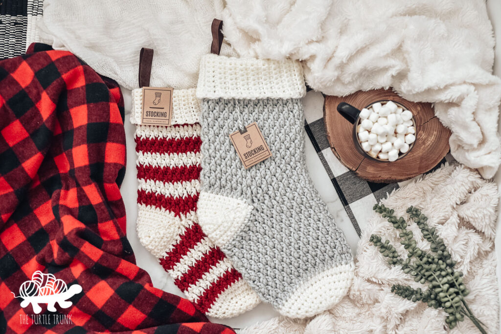 Photo shows 2 crochet Christmas stockings laying on a blanket. Crochet pattern is the Country Cottage Stocking by The Turtle Trunk.