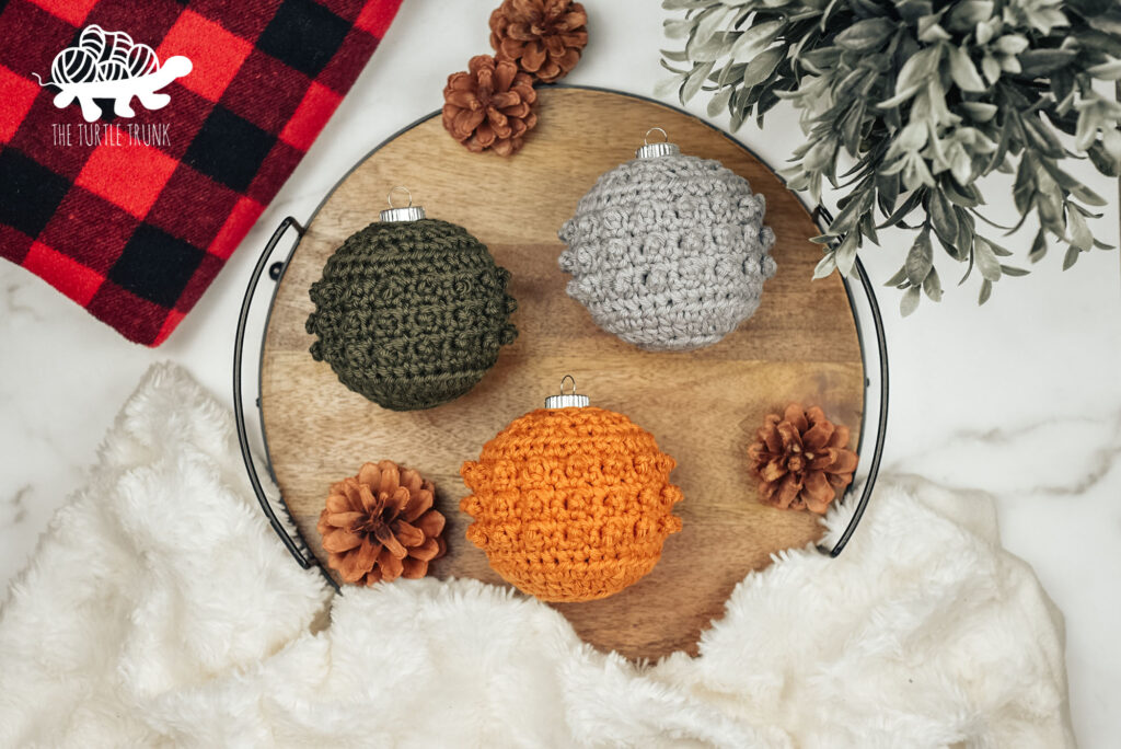 Photo shows 3 crochet Christmas ornaments laying on a wooden board. Crochet pattern is the Picot Tree Ornament by The Turtle Trunk.