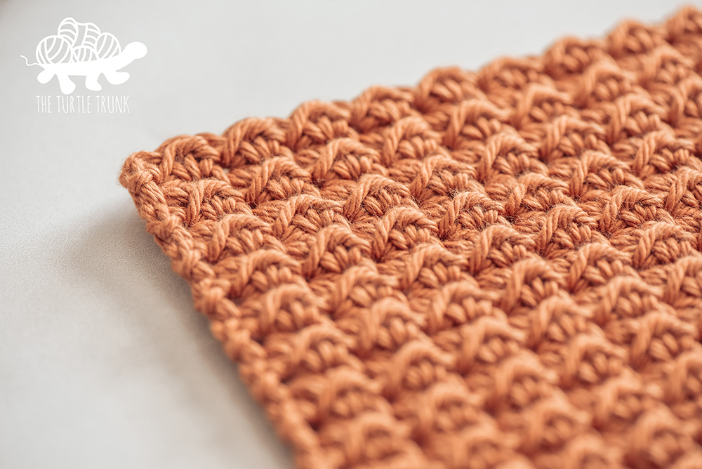 Photo shows a close up shot of an orange, crochet dish cloth laying on a white surface. Crochet pattern is the Farmhouse Dish Set by The Turtle Trunk.