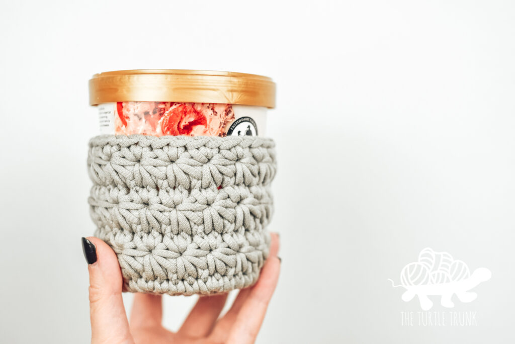 Hand holding an ice cream pint with a crochet cozy on it. All Star Ice Cream Pint Cozy crochet pattern by The Turtle Trunk