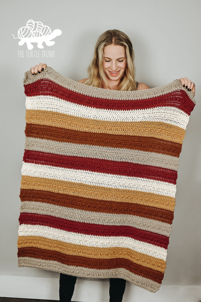 Woman holding a striped, crochet Picot Blanket. Pattern by The Turtle Trunk.