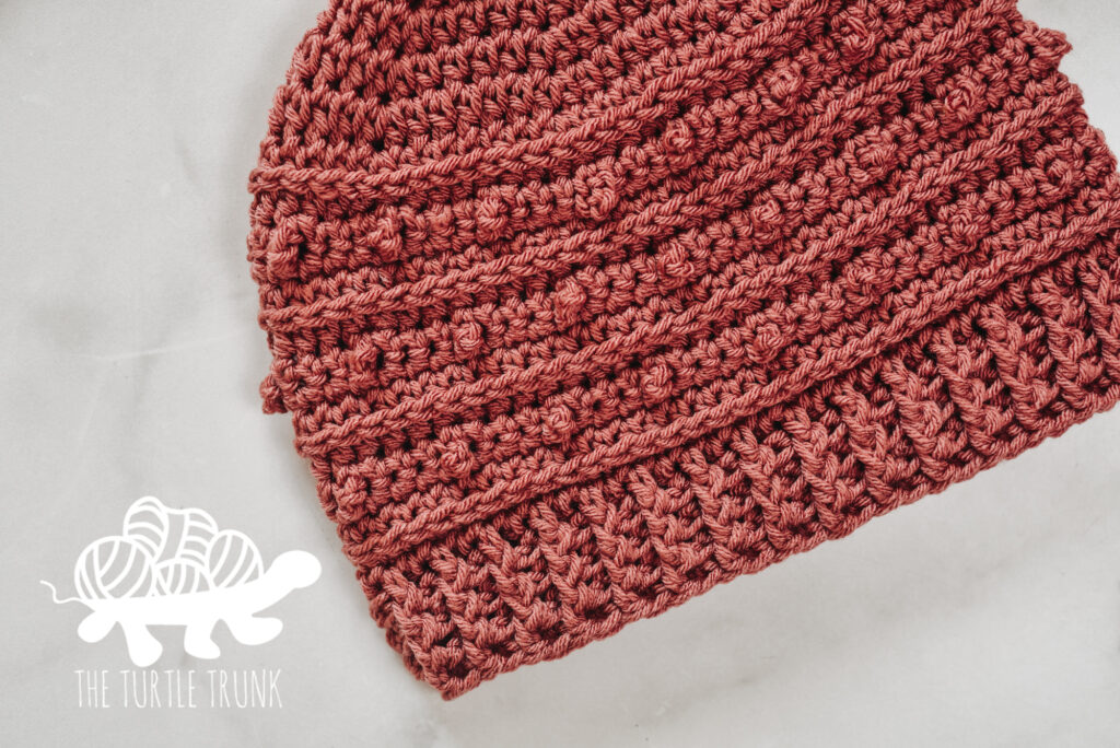 A pink crochet beanie lays on a white surface. Picot Beanie crochet pattern by The Turtle Trunk.