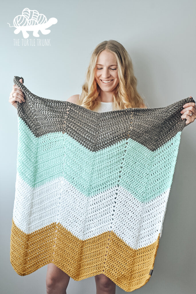 Woman holding a Bebe Baby Blanket in the colors taupe, teal, white, and yellow.