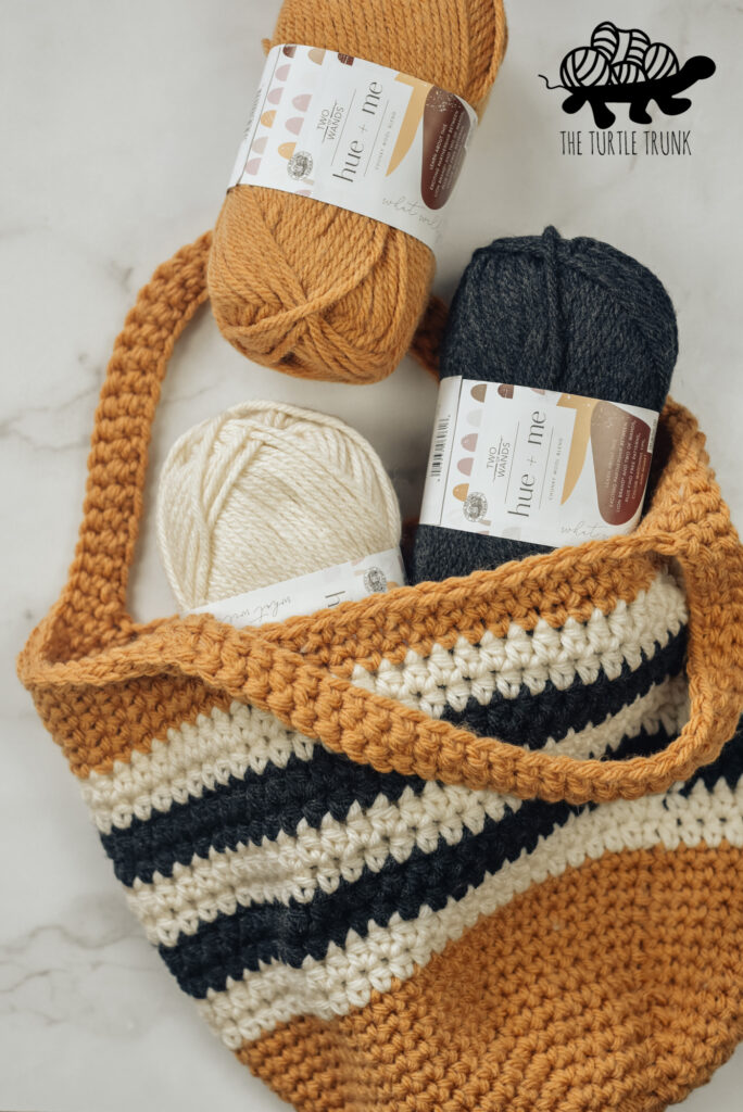 Yellow, black, and white crochet bag laying on a white surface with 3 skeins of matching yarn coming out of the bag.