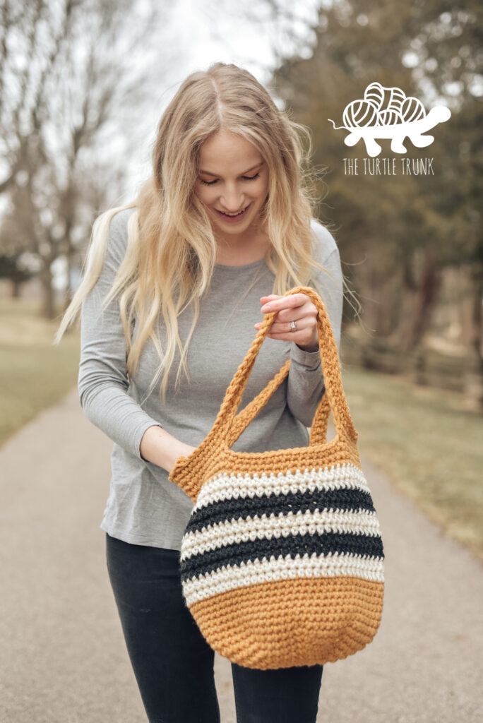 Woman standing outside holding a yellow, black, and white crochet tote bag.