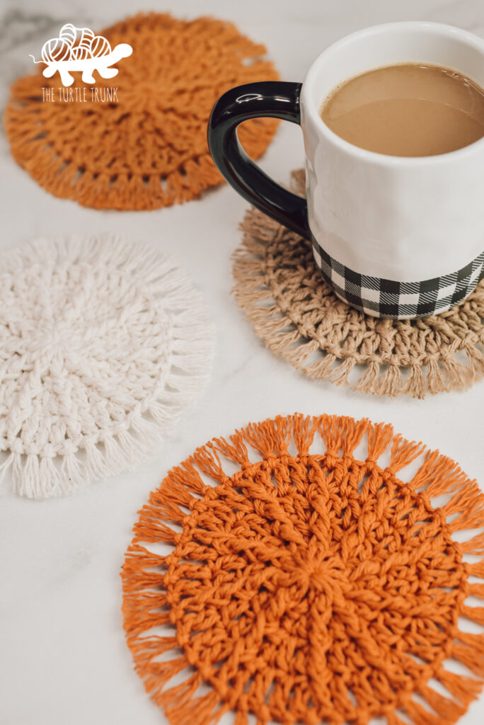 4 crochet coasters laying on a white surface. A coffee mug sits on one of the coasters. Hello Sunshine Coaster crochet pattern by The Turtle Trunk.