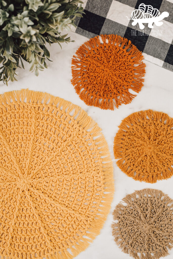 Photo shows a crochet placemat and matching crochet coasters laying on a white surface. Crochet patterns are the Hello Sunshine Placemat and Hello Sunshine Coaster by The Turtle Trunk.