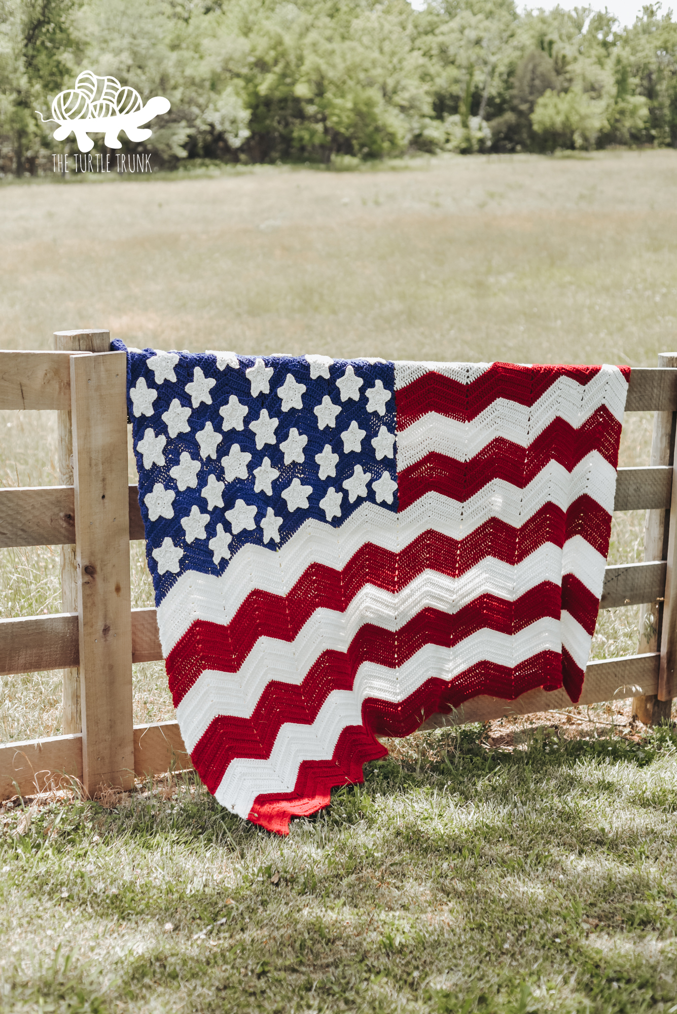 Photo shows a crochet American Flag Blanket hanging on a fence outside. Crochet pattern is the American Flag Blanket by The Turtle Trunk.