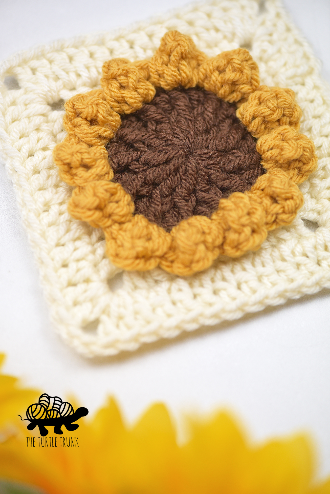 A crochet square with a sunflower laying on a white surface. Crochet pattern is the Sunflower Square by The Turtle Trunk.