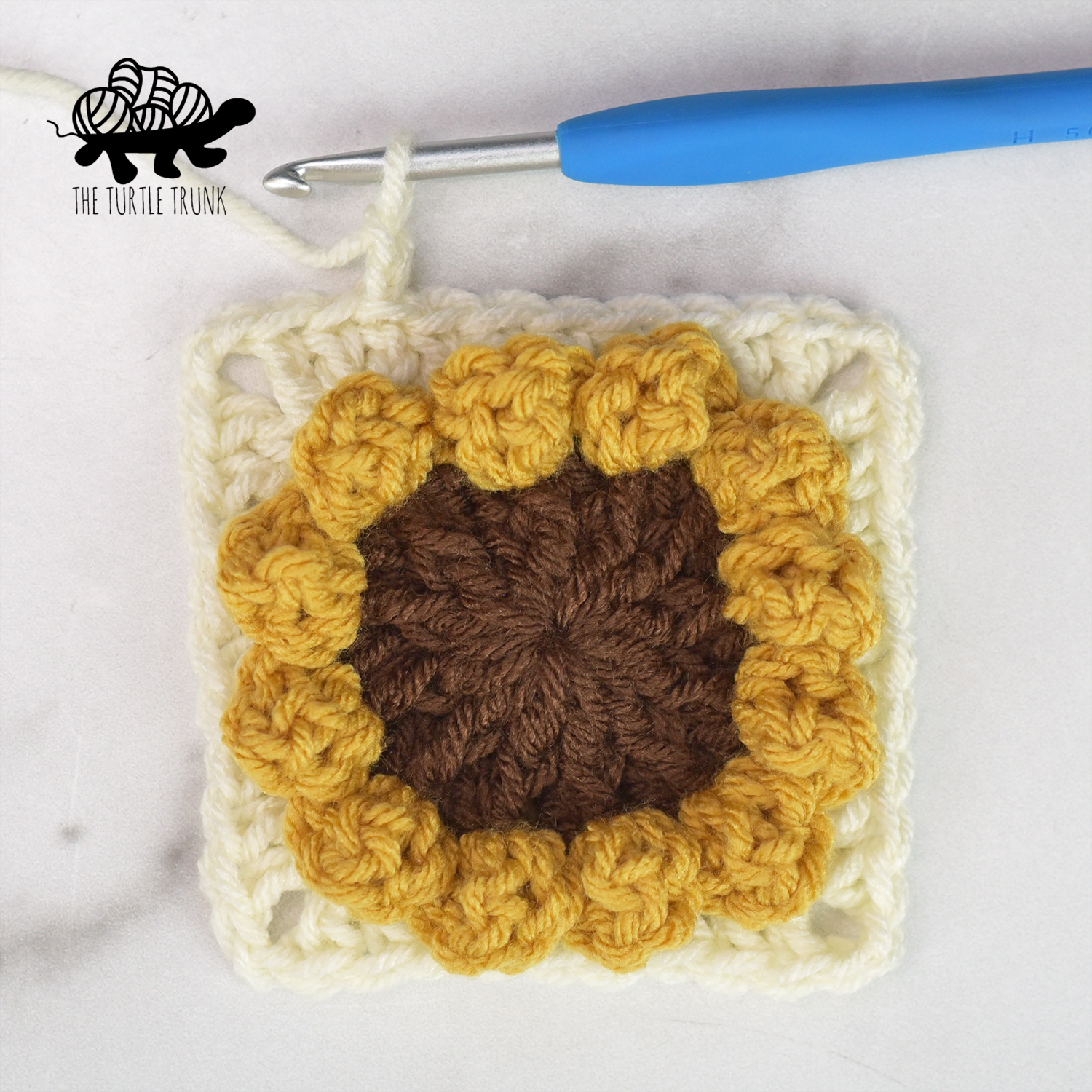 The sunflower square after round 4. Shows a crochet sunflower with one square border row around it.