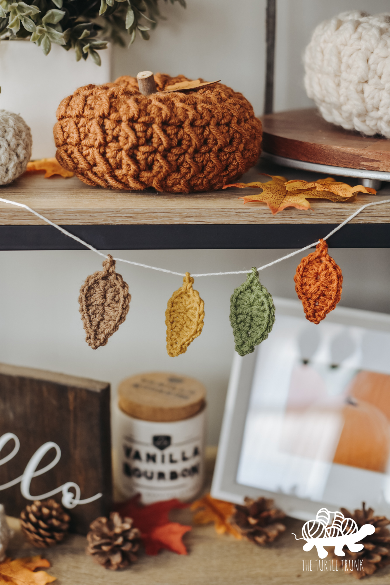 Photo shows a shelf decorated with Fall themed items, like crochet pumpkins. Hanging off the shelf is a garland with crochet leaves on it.