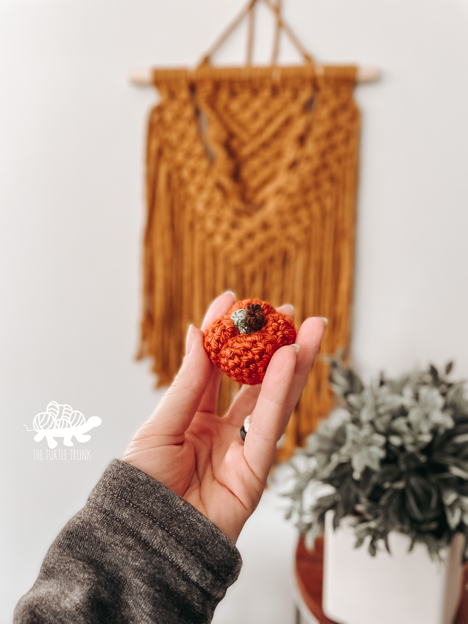 Photo shows a woman's hand holding a mini, crochet pumpkin. Mini Pumpkin crochet pattern by The Turtle Trunk.