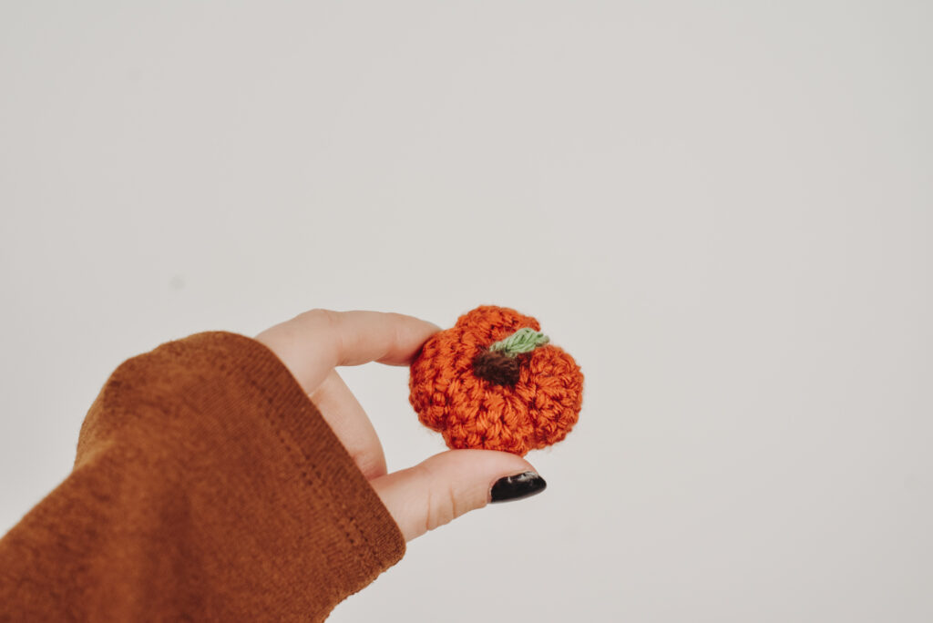 Photo shows a hand holding a mini crochet pumpkin. Mini Pumpkin crochet pattern by The Turtle Trunk.