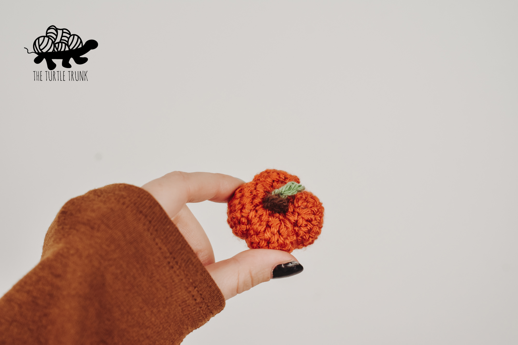 Photo shows a hand holding a mini crochet pumpkin. Mini Pumpkin crochet pattern by The Turtle Trunk.