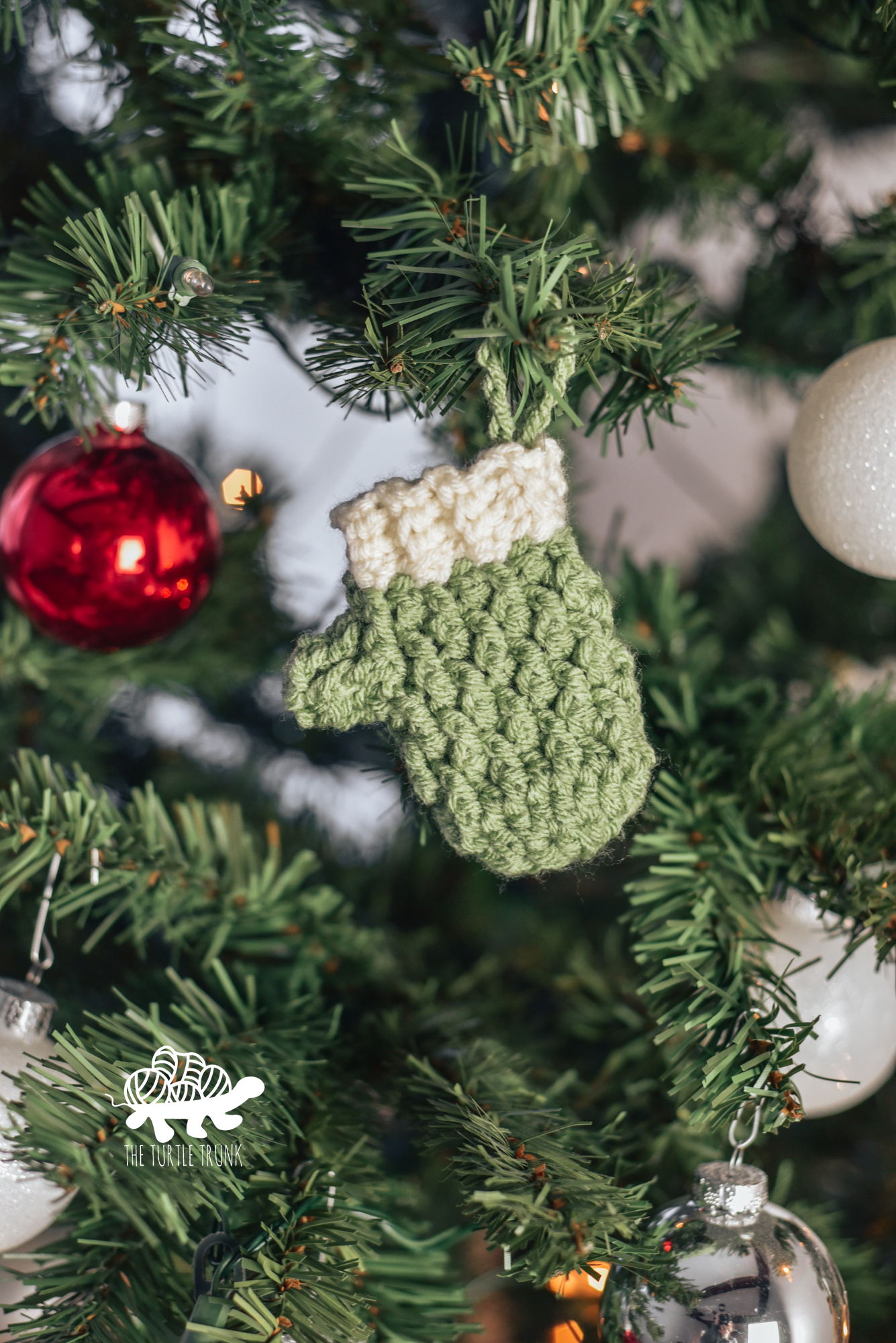 Photo shows a mini crochet mitten hanging on a Christmas Tree. Crochet pattern is the Mini Country Cottage Mitten by The Turtle Trunk.