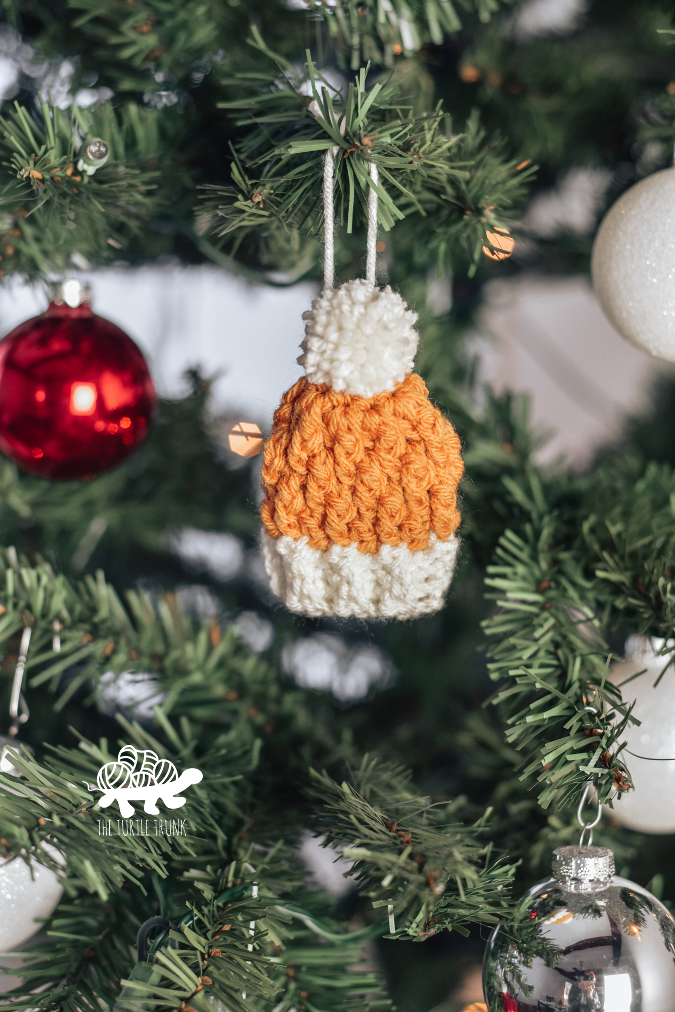 Photo shows a mini crochet beanie ornament hanging on a Christmas tree. Crochet pattern is the Mini Country Cottage Beanie by The Turtle Trunk.