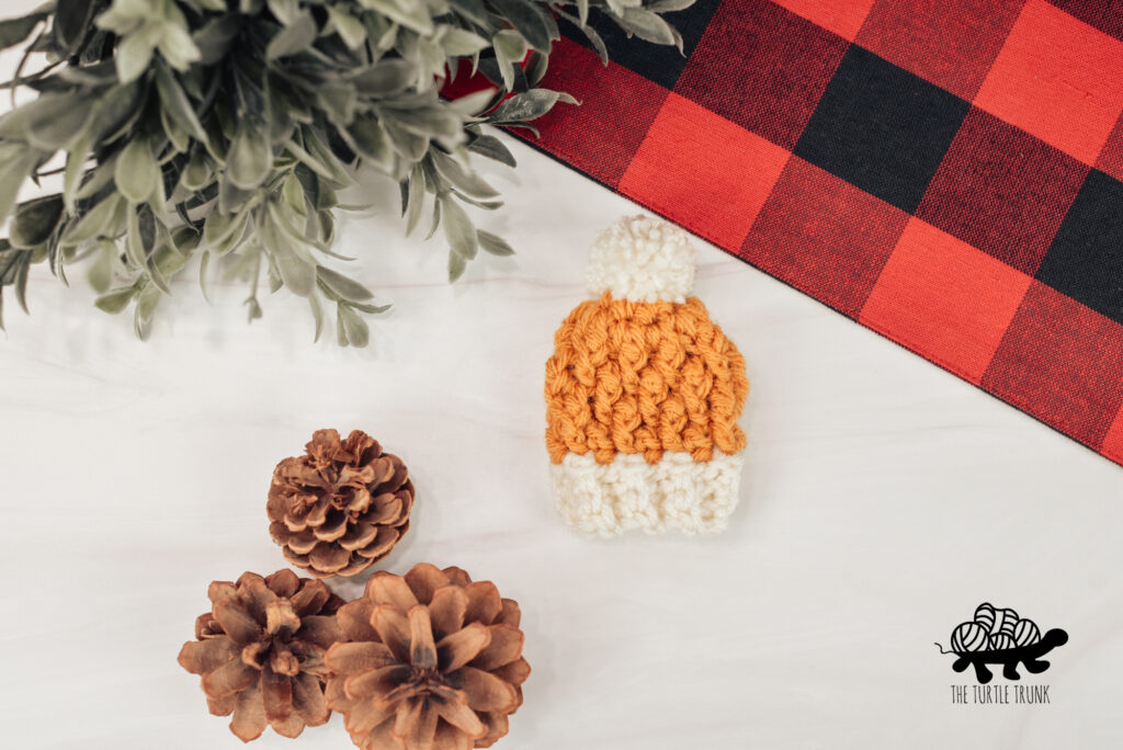 Photo shows a mini crochet beanie laying on a white surface. Crochet pattern is the Mini Country Cottage Beanie by The Turtle Trunk.