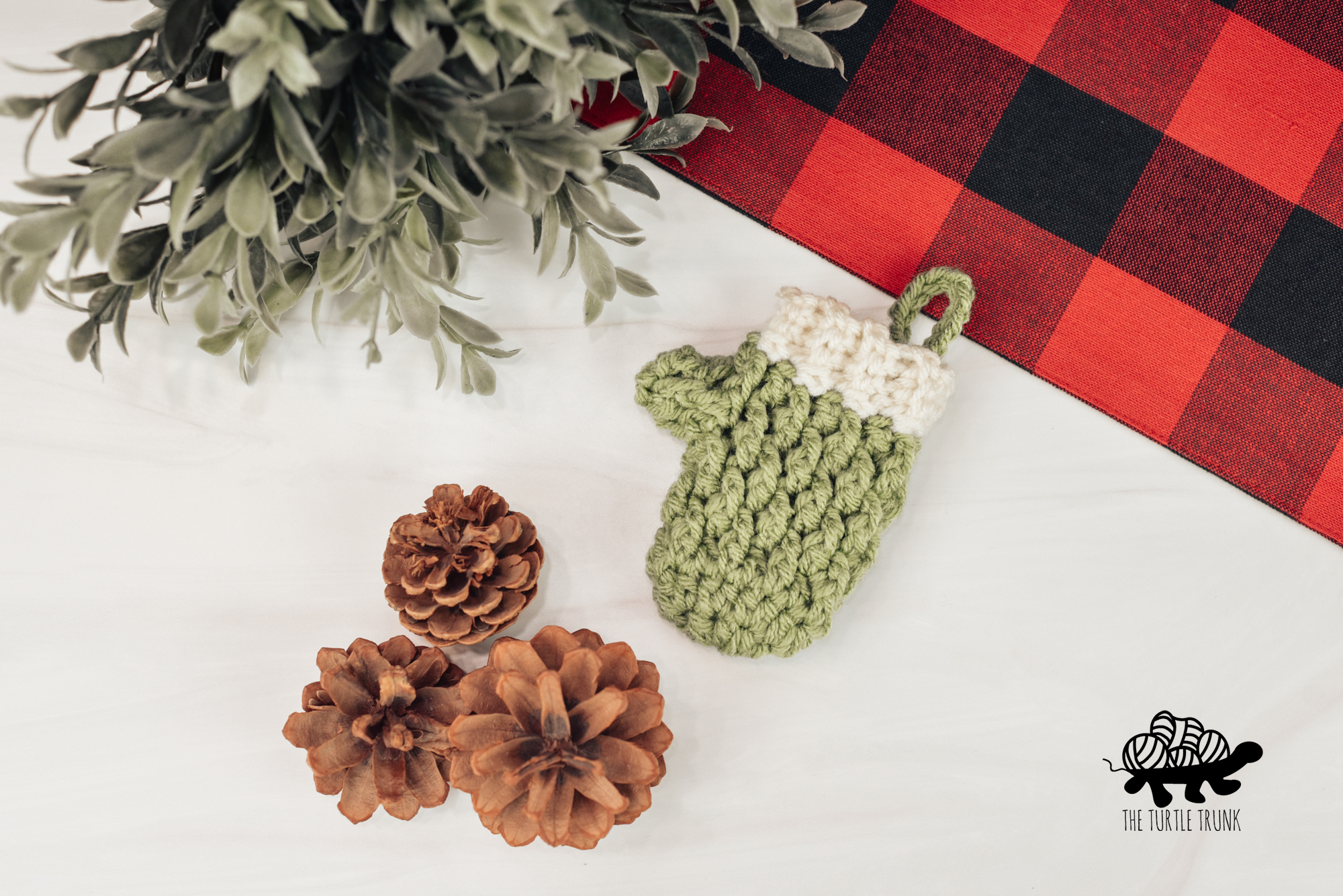 Photo shows a mini crochet mitten laying on a white surface. Crochet pattern is the Mini Country Cottage Mitten by The Turtle Trunk.