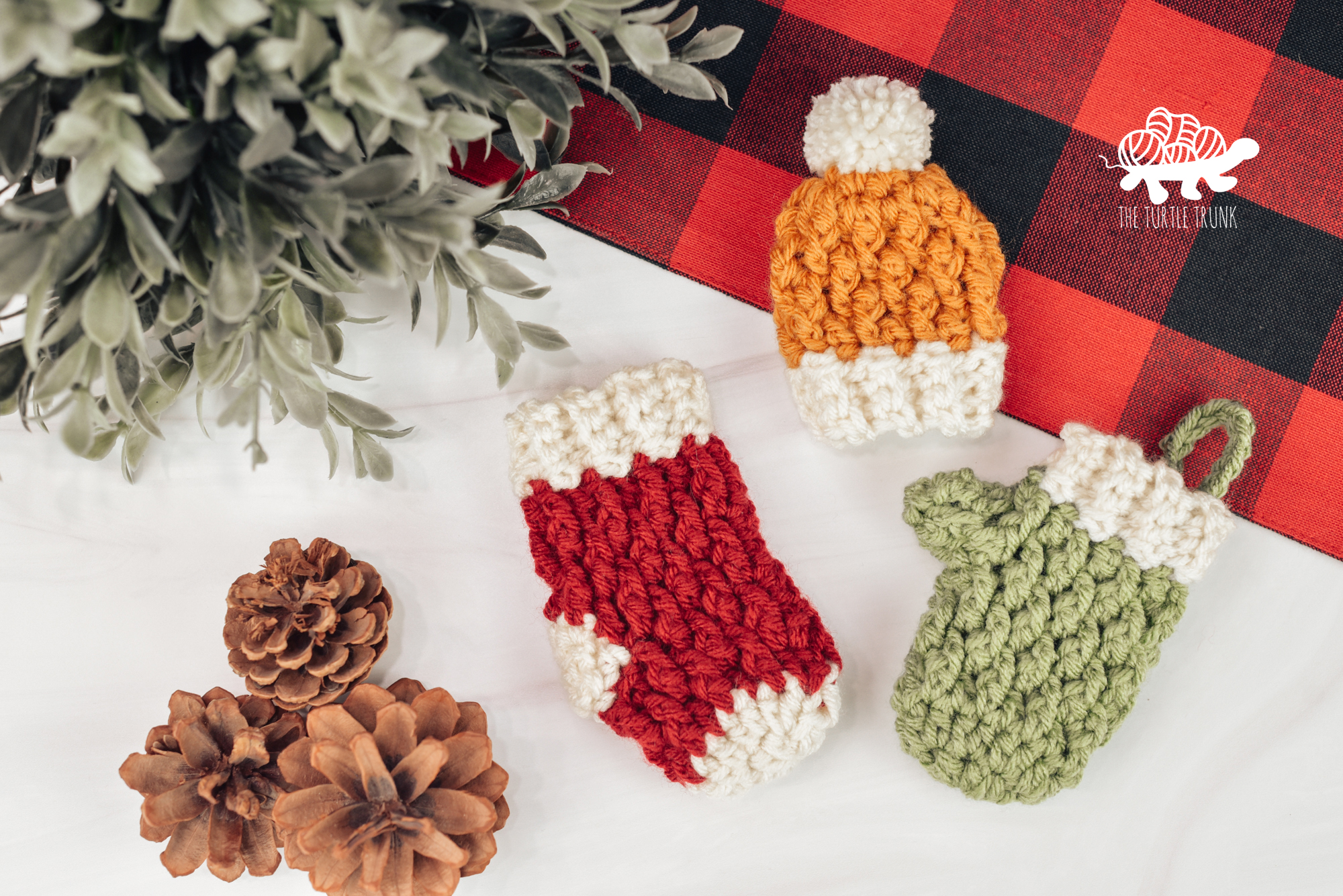 Photo shows a mini crochet stocking, beanie, and mitten laying on a white surface. Crochet pattern is the Country Cottage Minis by The Turtle Trunk.