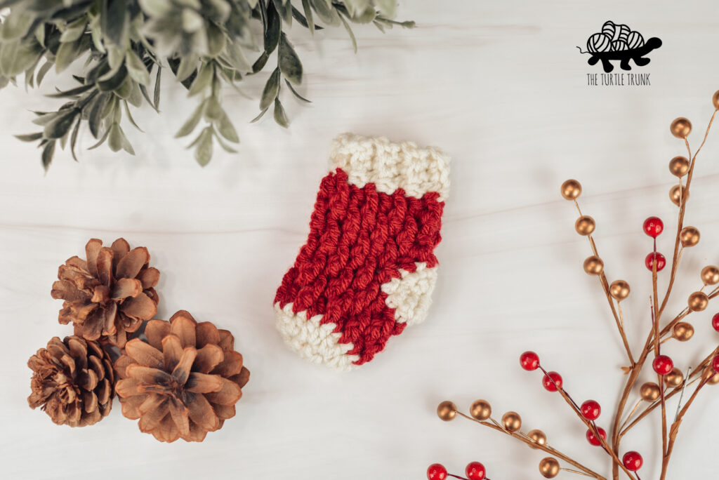 Photo shows a mini crochet stocking laying on a white surface.