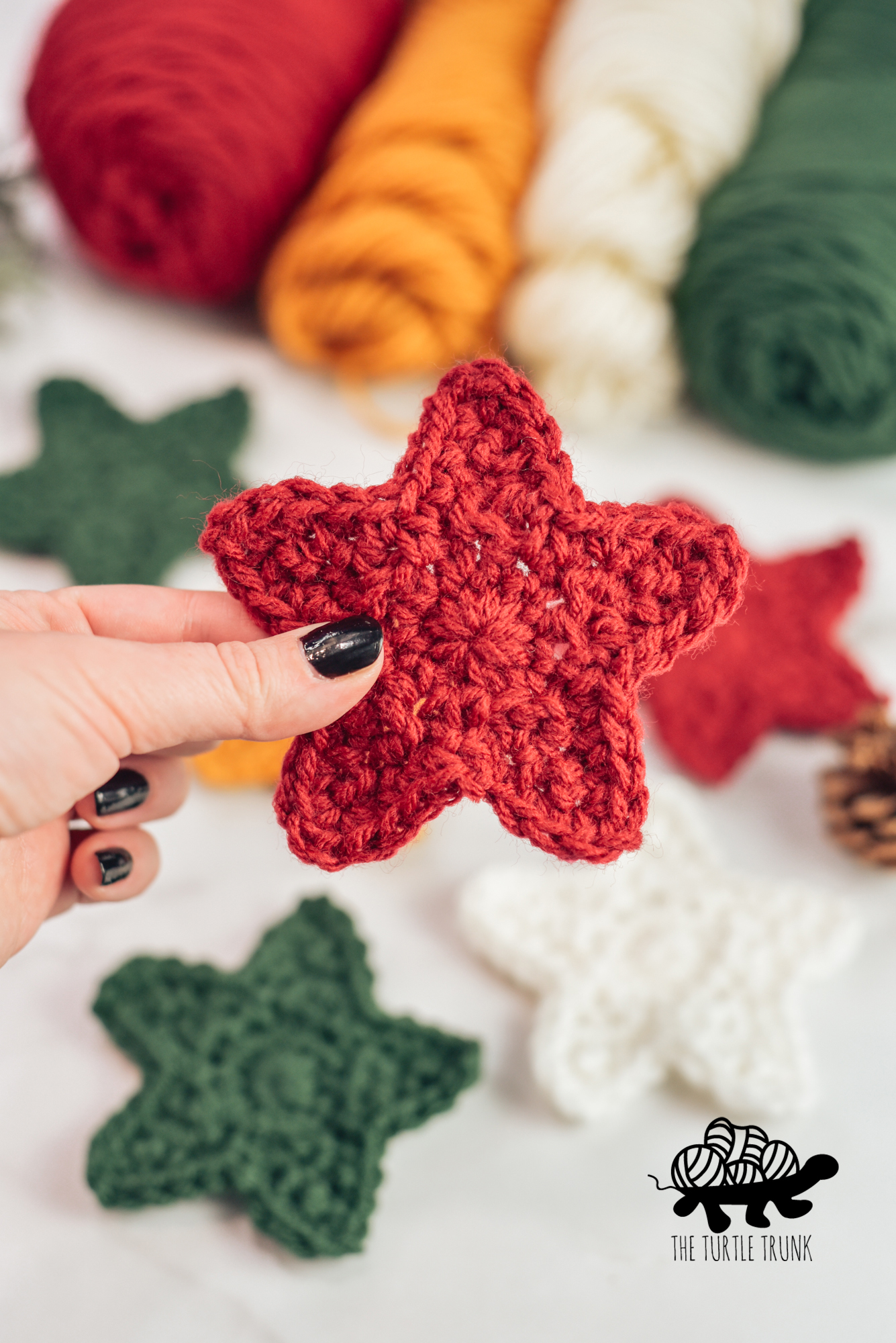 Photo shows a hand holding a red crochet star. Star crochet pattern by The Turtle Trunk.