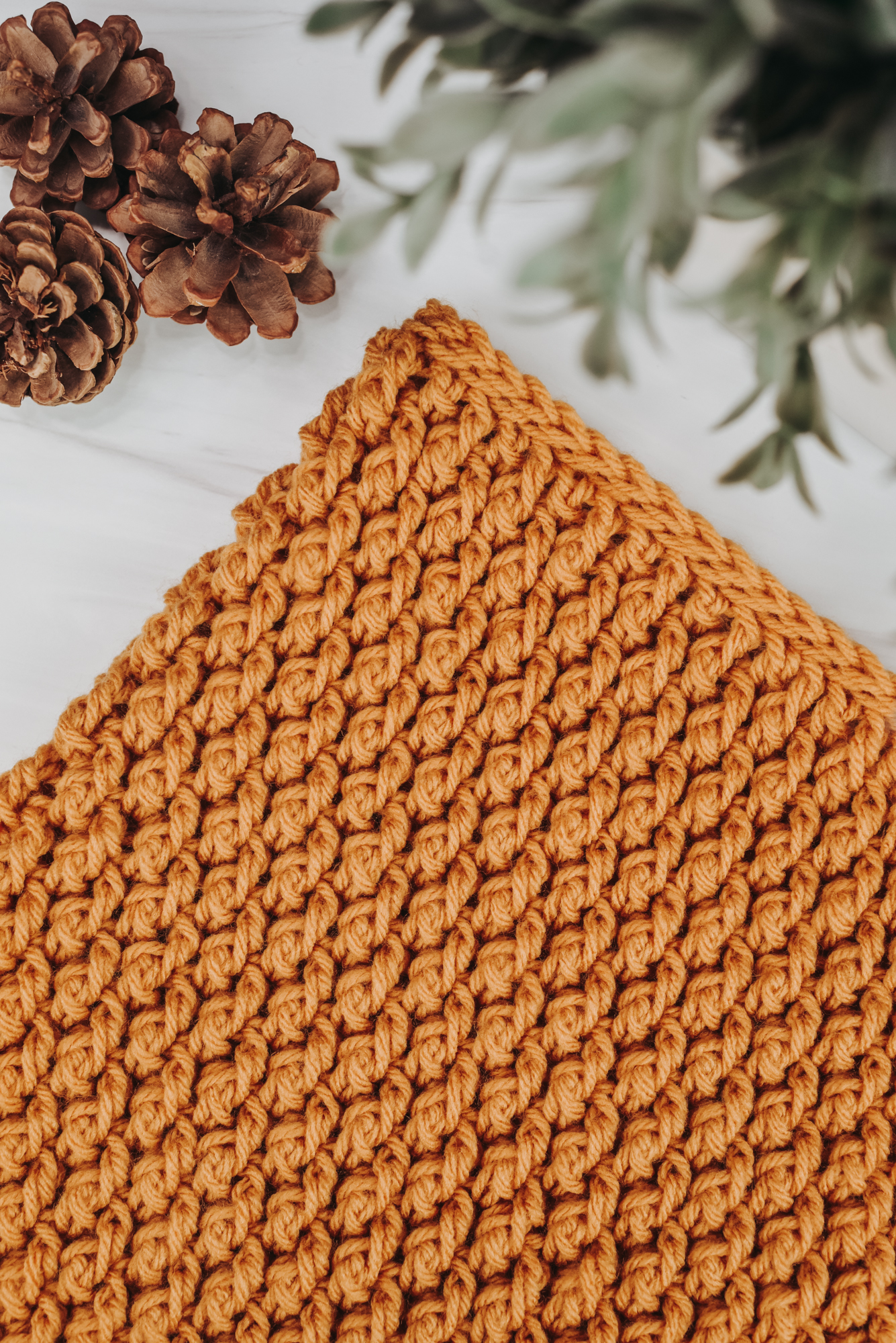 Photo shows a close up of a yellow, crochet cowl, laying on a white surface. Crochet pattern is the Country Cottage Cowl by The Turtle Trunk.