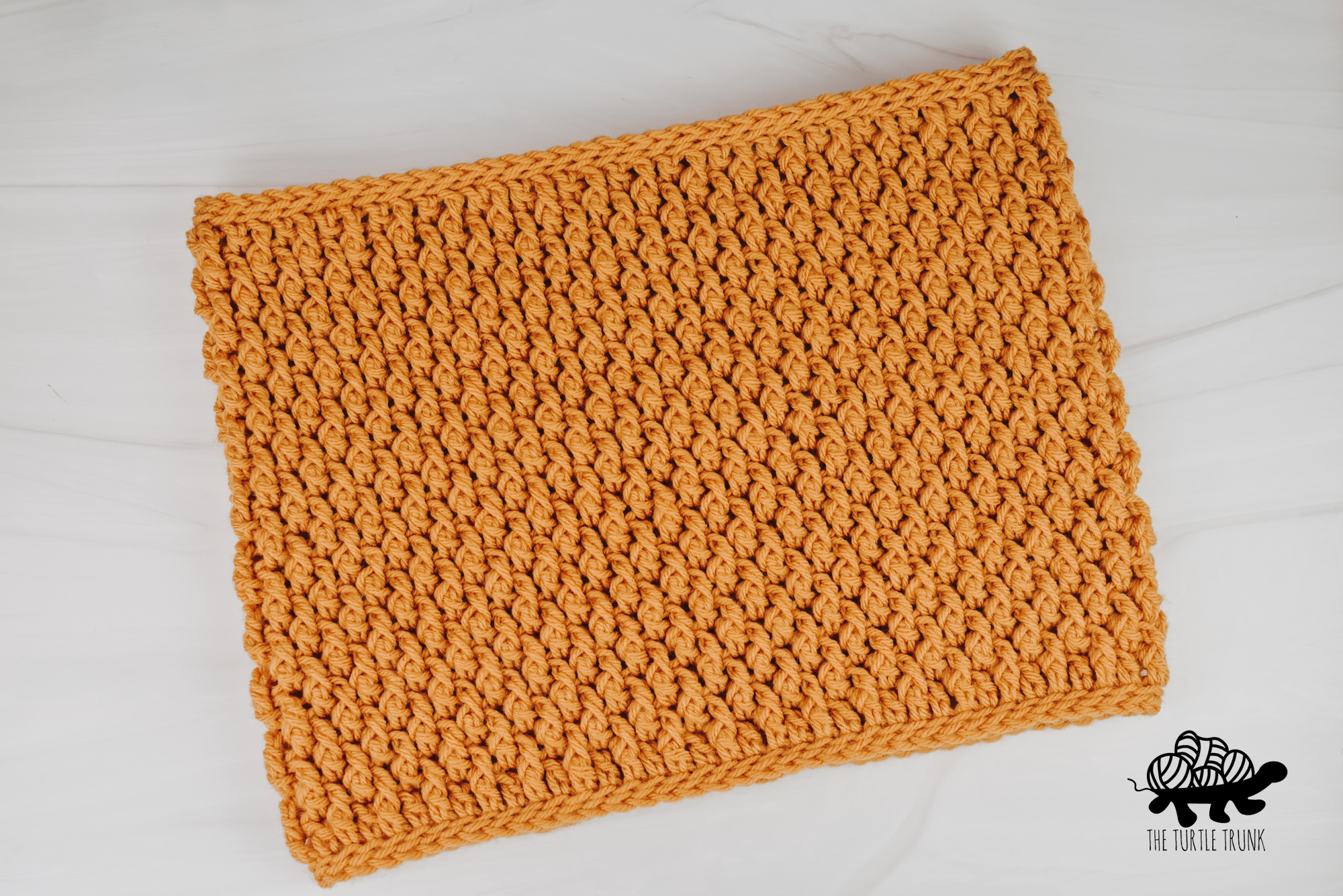 Photo shows a yellow, crochet cowl laying on a white surface.