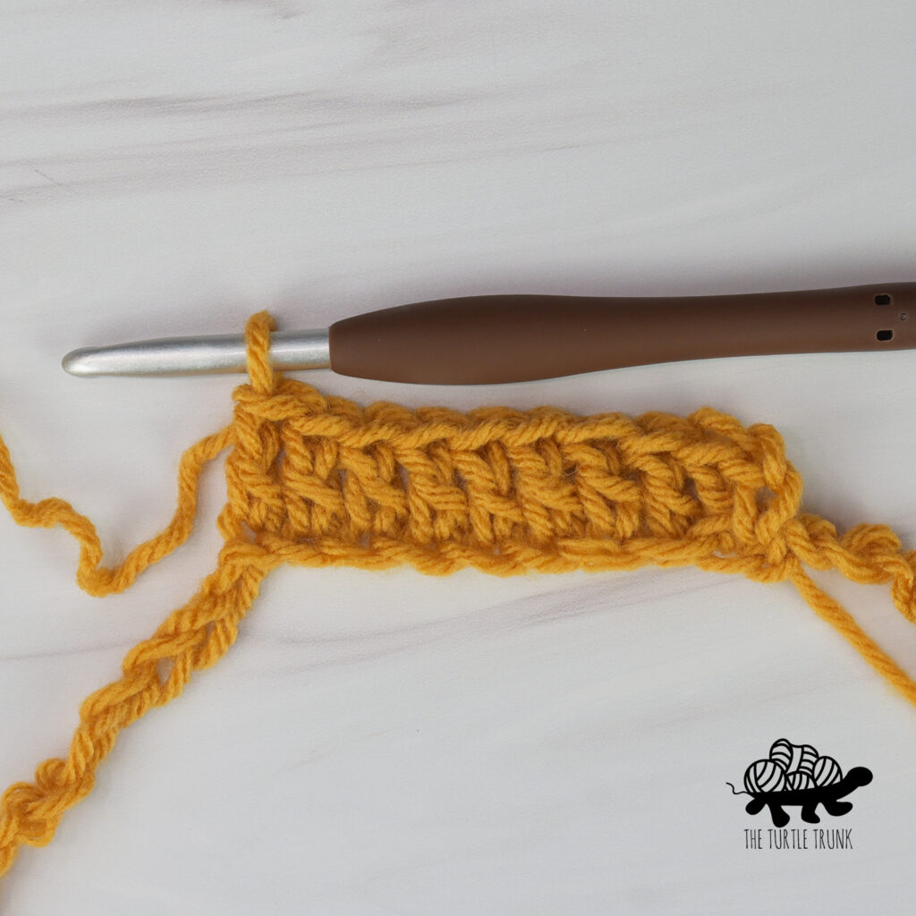 Photo shows a crochet foundation chain with double crochet stitches worked into it with yellow yarn.