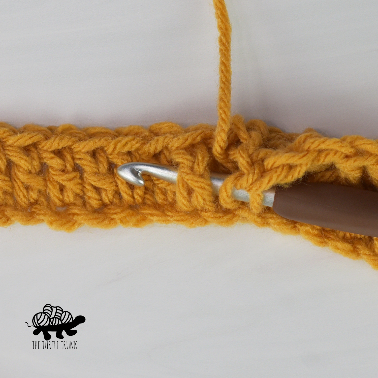 Photo shows a crochet hook around the back of a stitch to show how to crochet a front post double crochet stitch with yellow yarn.