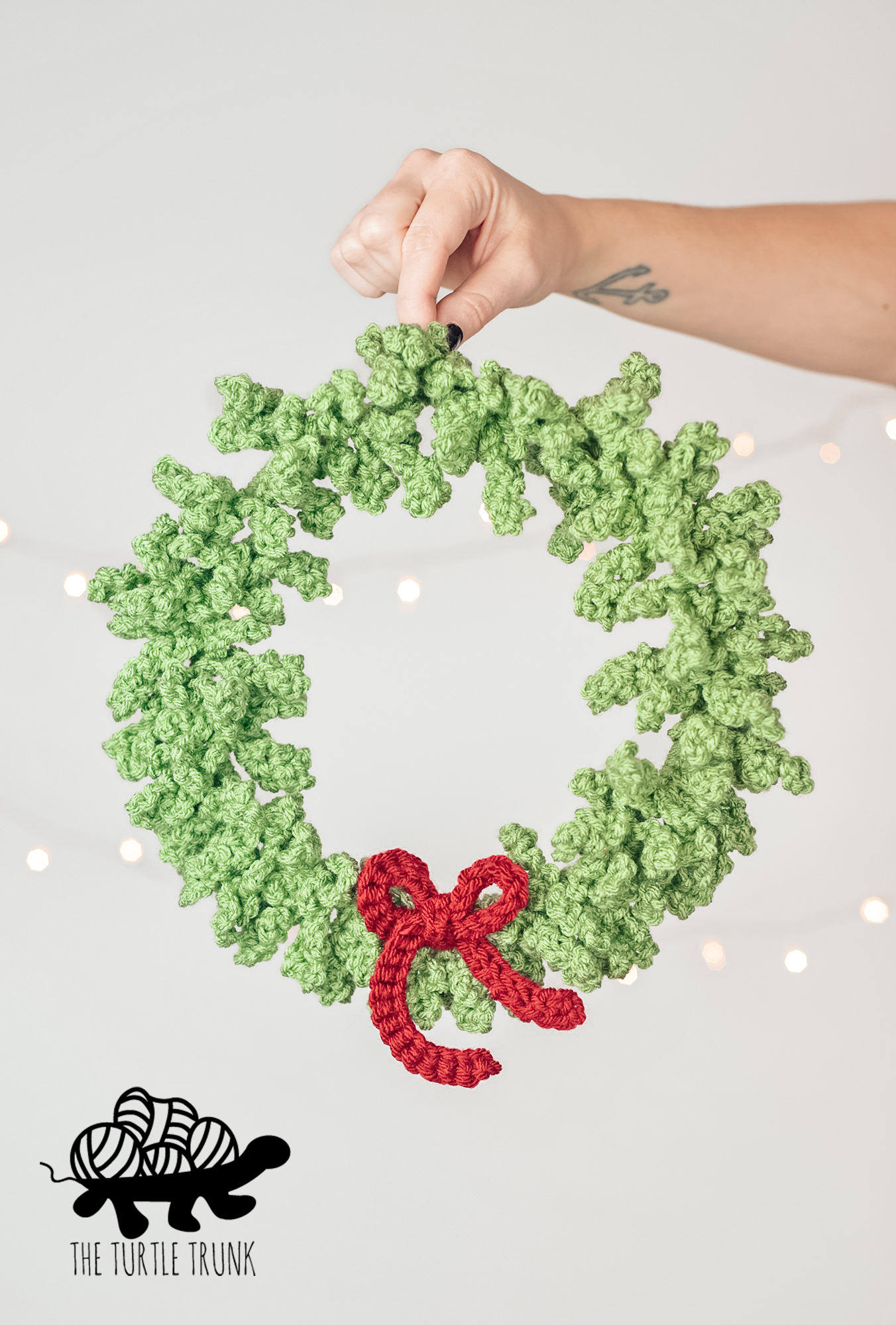 Photo shows a hand holding a crochet wreath with lights in the background. Crochet pattern is the Hp