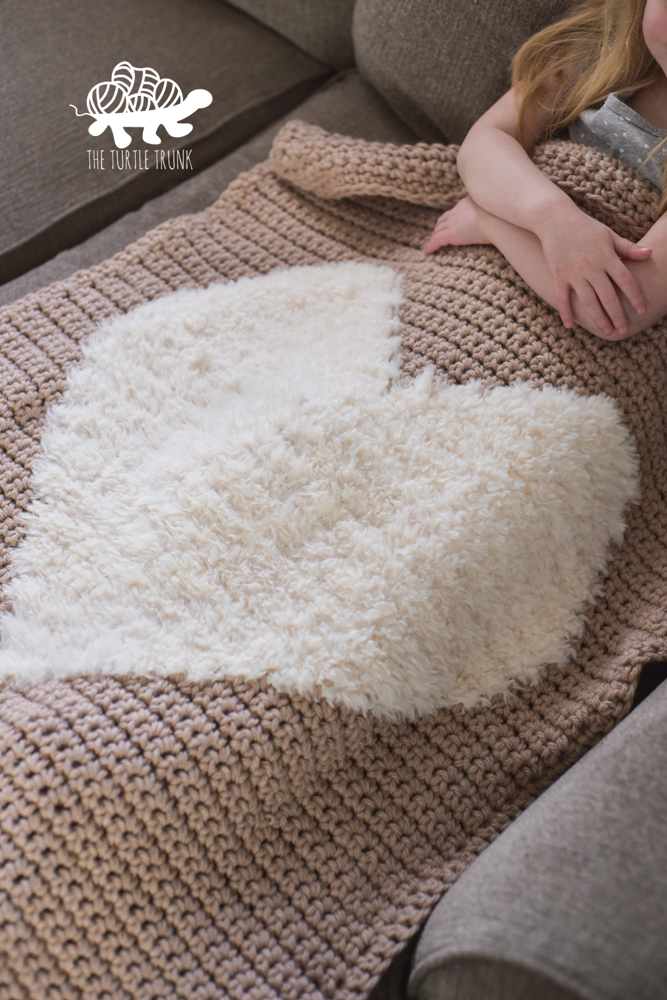 Photo shows a young girl laying on a couch with a crochet blanket on her lap. The crochet blanket features a faux fur heart in the center. Crochet pattern is the Love to Cuddle Blanket by The Turtle Trunk.