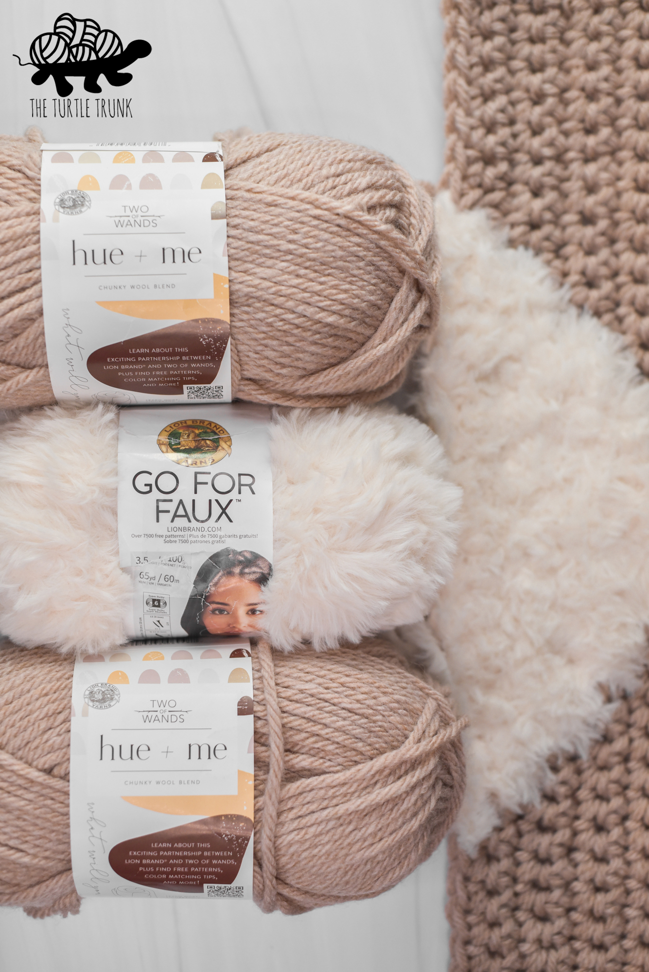 Photo shows 3 skeins of yarn laying on a white background. The yarns are Lion Brand Yarn hue and Me in the color Desert and Lion Brand Yarn Go For Faux in the color Baked Alaska.