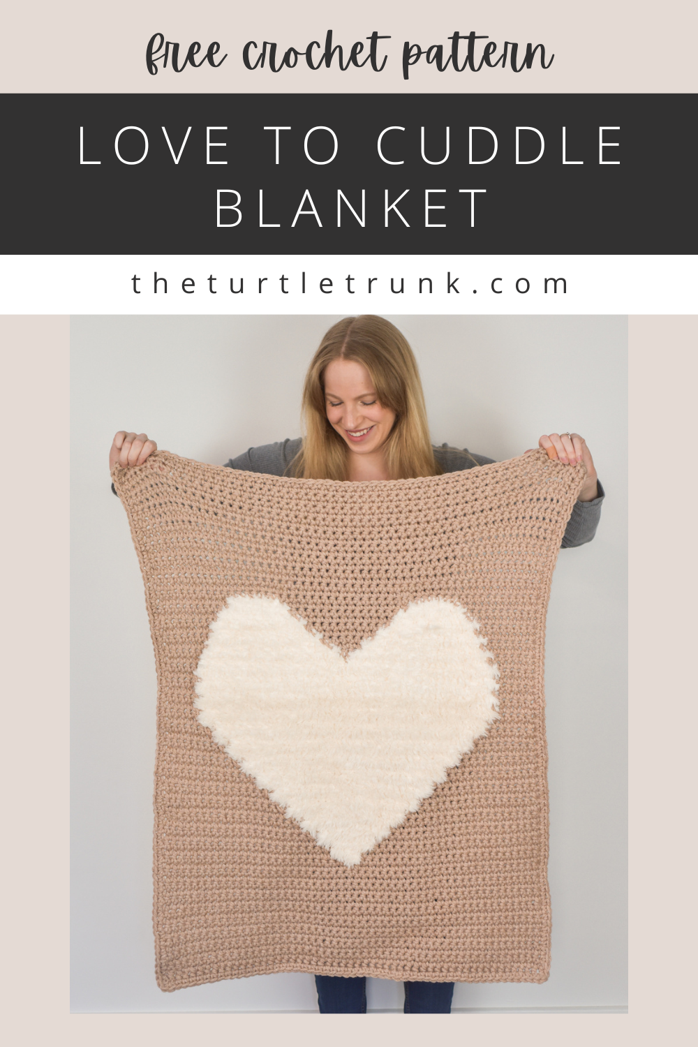 Photo shows a woman holding up a crochet blanket with a. faux fur heart on it. Crochet pattern is the Love to Cuddle Blanket by The Turtle Trunk.