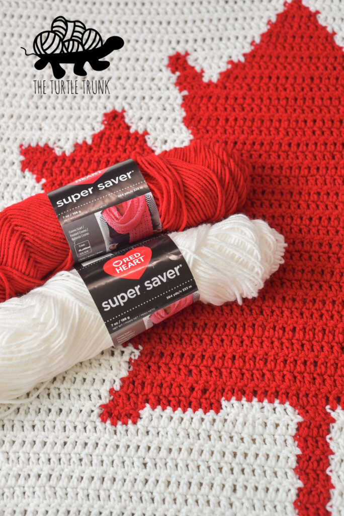 Closeup of red and white yarn and a crochet Canadian Flag Blanket.