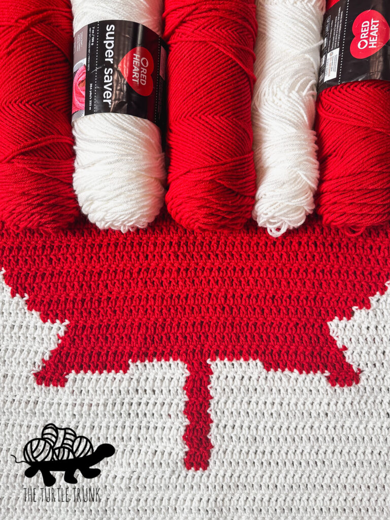 Closeup of red and white yarn and a crochet Canadian Flag Blanket.