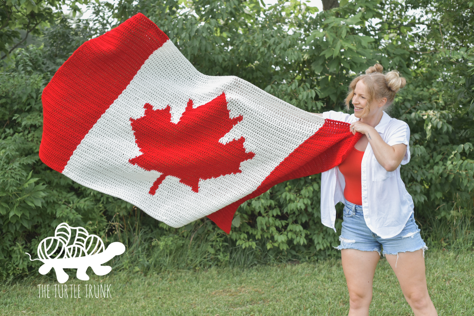 Women standing outside, tossing up a crochet blanket that looks like the Canadian Flag. Crochet pattern is the Canadian Flag Blanket by The Turtle Trunk.