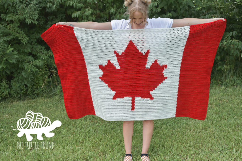 Woman holding up a crochet Canadian Flag Blanket.