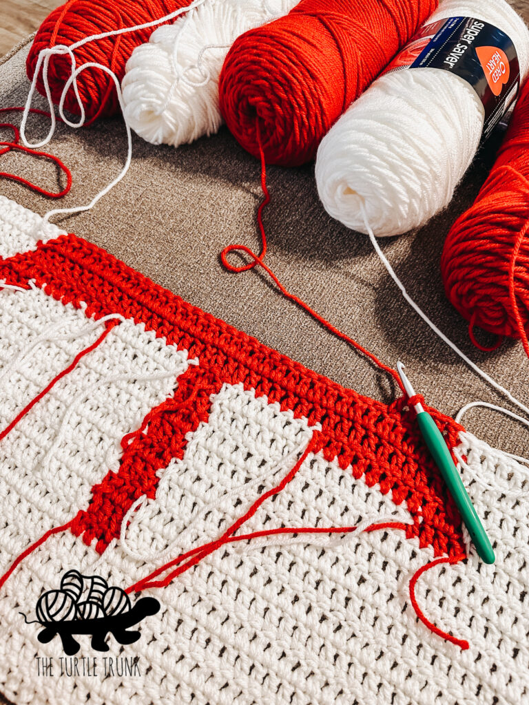 Closeup of red and white yarn and a crochet Canadian Flag Blanket.