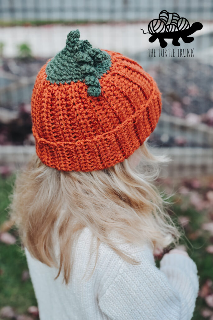 A child wearing a ribbed crochet hat that looks like a pumpkin.