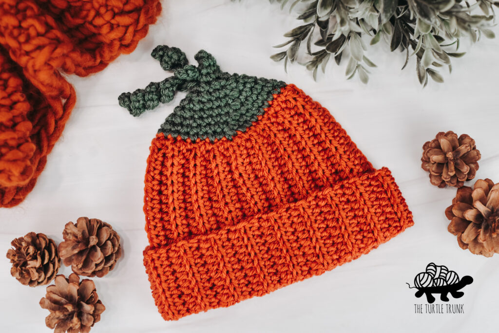 A crochet pumpkin beanie laying on a white surface. 