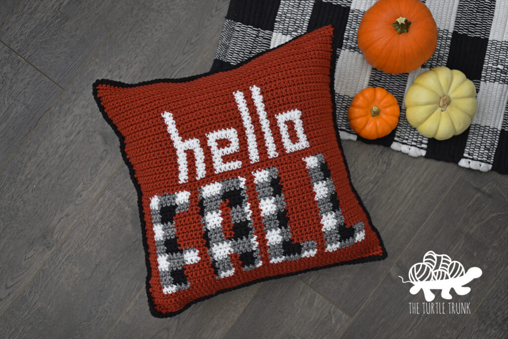 Photo shows a crochet pillow that says Hello Fall on it, laying on the floor.