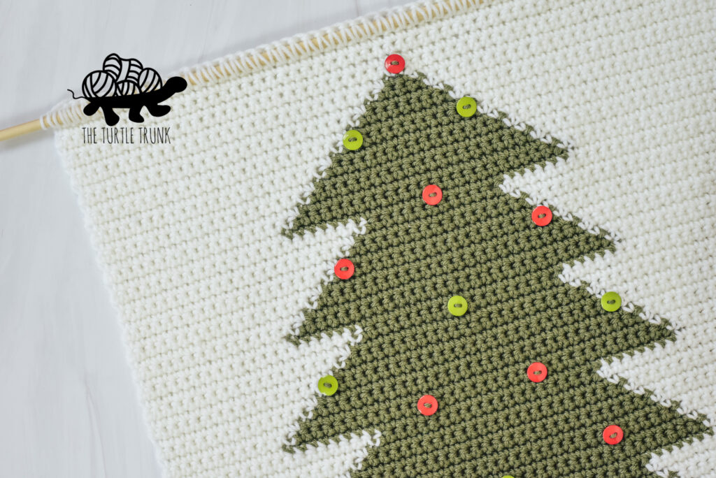 Photo shows a crochet wall hanging that features a green tree with red and green buttons sewn on it.