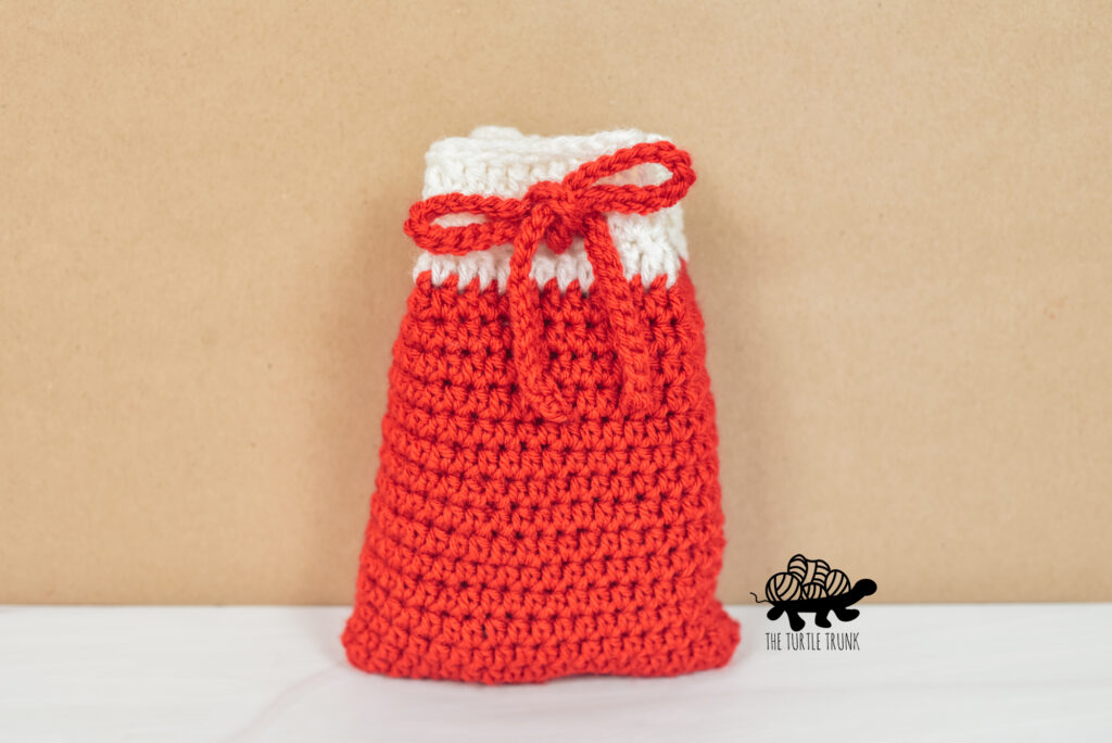 Photo shows a small, red and white crochet bag, that features a drawstring closure.